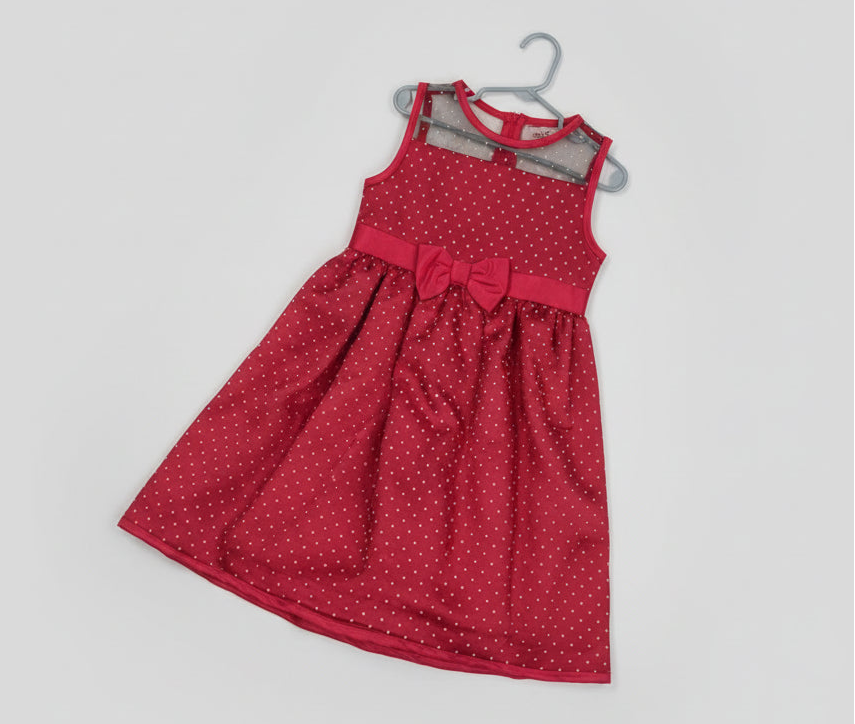 Red polka dot dress with a bow on a hanger against a colorful background