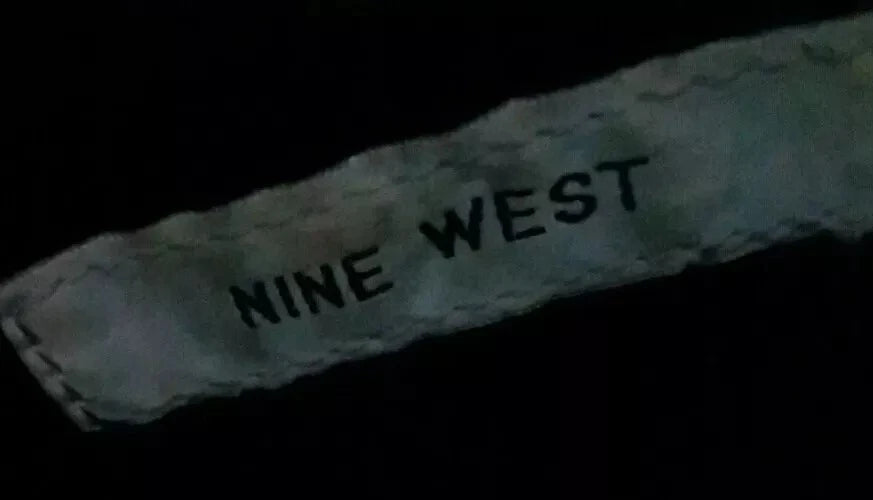 Text 'NINE WEST' on a textured surface with a dark background