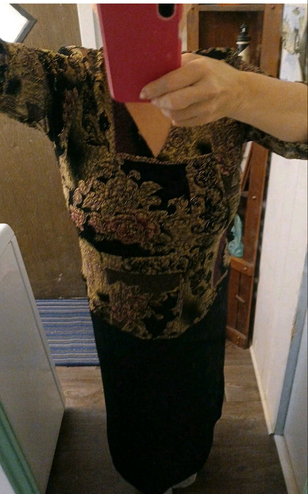 Person holding a red phone case with a patterned shirt and skitr in a room.