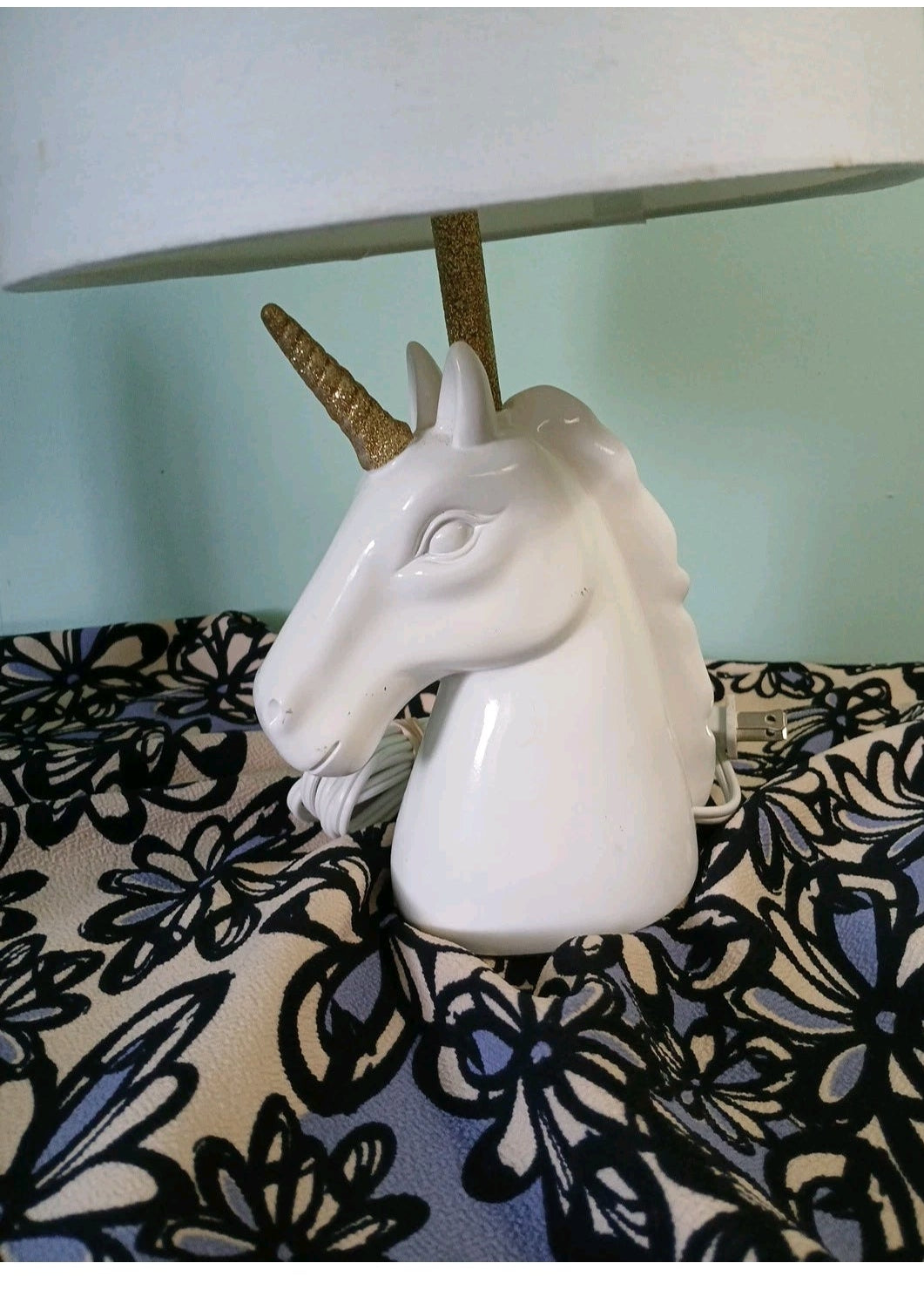 Unicorn-shaped lamp on a floral-patterned surface with a light blue background