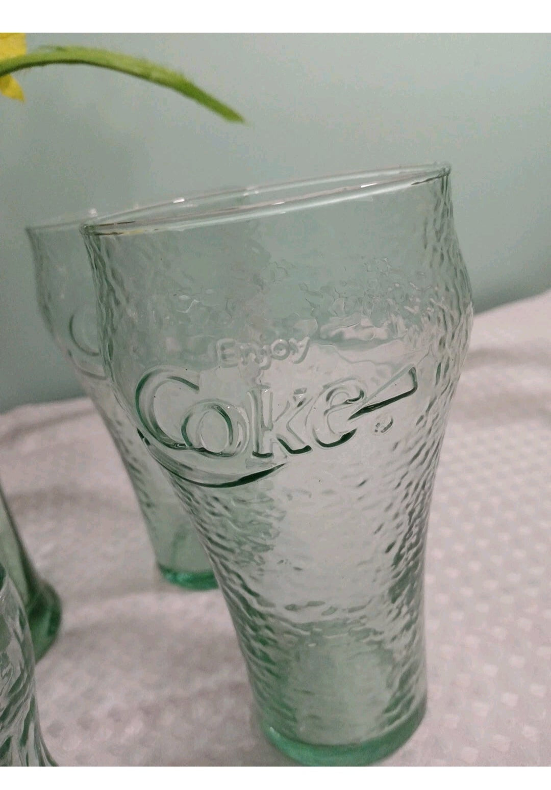 Clear Coca-Cola glass on a textured surface with a light gray background