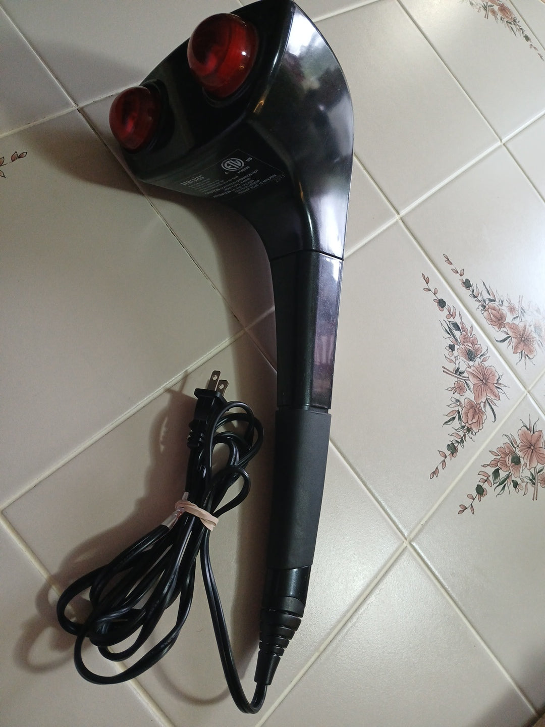 Black massager with red buttons on a tiled floor