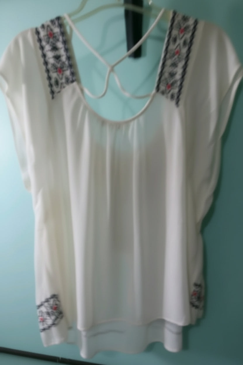 White blouse with embroidery on a hanger against a light blue wall