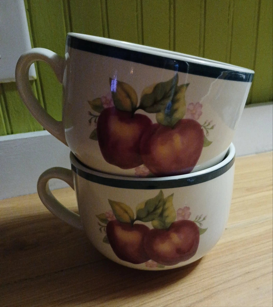 Two stacked ceramic mugs with fruit design on a wooden surface.