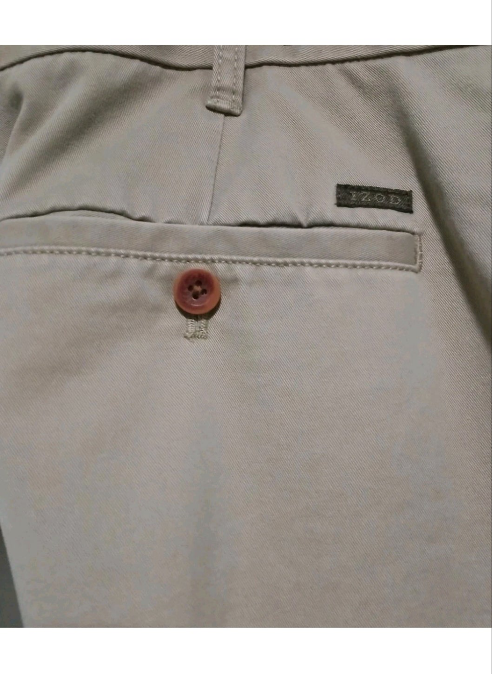 Close-up of beige pants with a button and brand label.