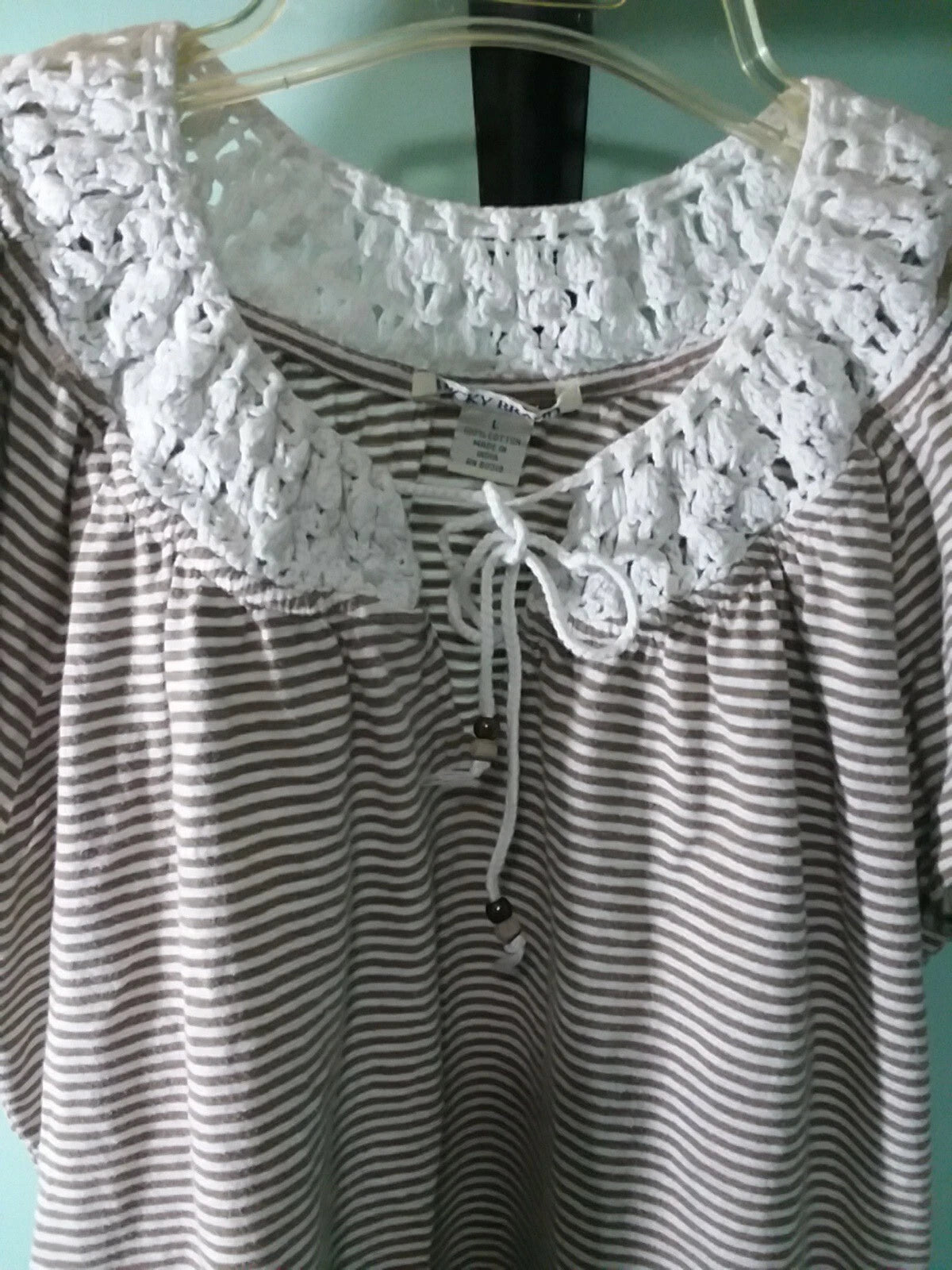 Striped shirt with lace details on a hanger against a light blue wall