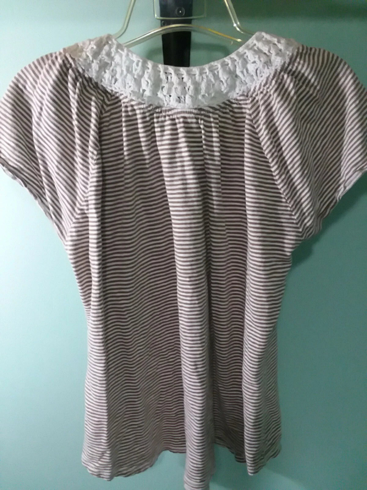 Striped blouse with lace neckline on a hanger against a teal wall