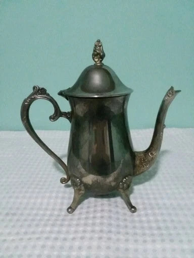 Vintage silver teapot on a textured surface with a light blue background