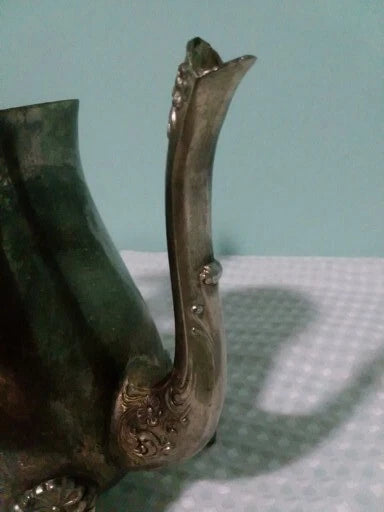 Decorative metal teaspout on a  te pot  textured surface with a light blue background