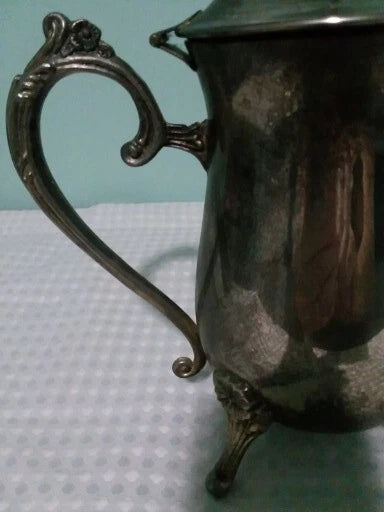 Silver pitcher with ornate handle on a textured surface