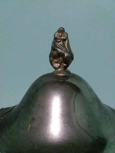 Close-up of a metallic object with a decorative finial on a light blue background