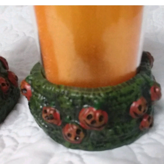 Decorative candle holder with green base and red pumpkin designs on a white background