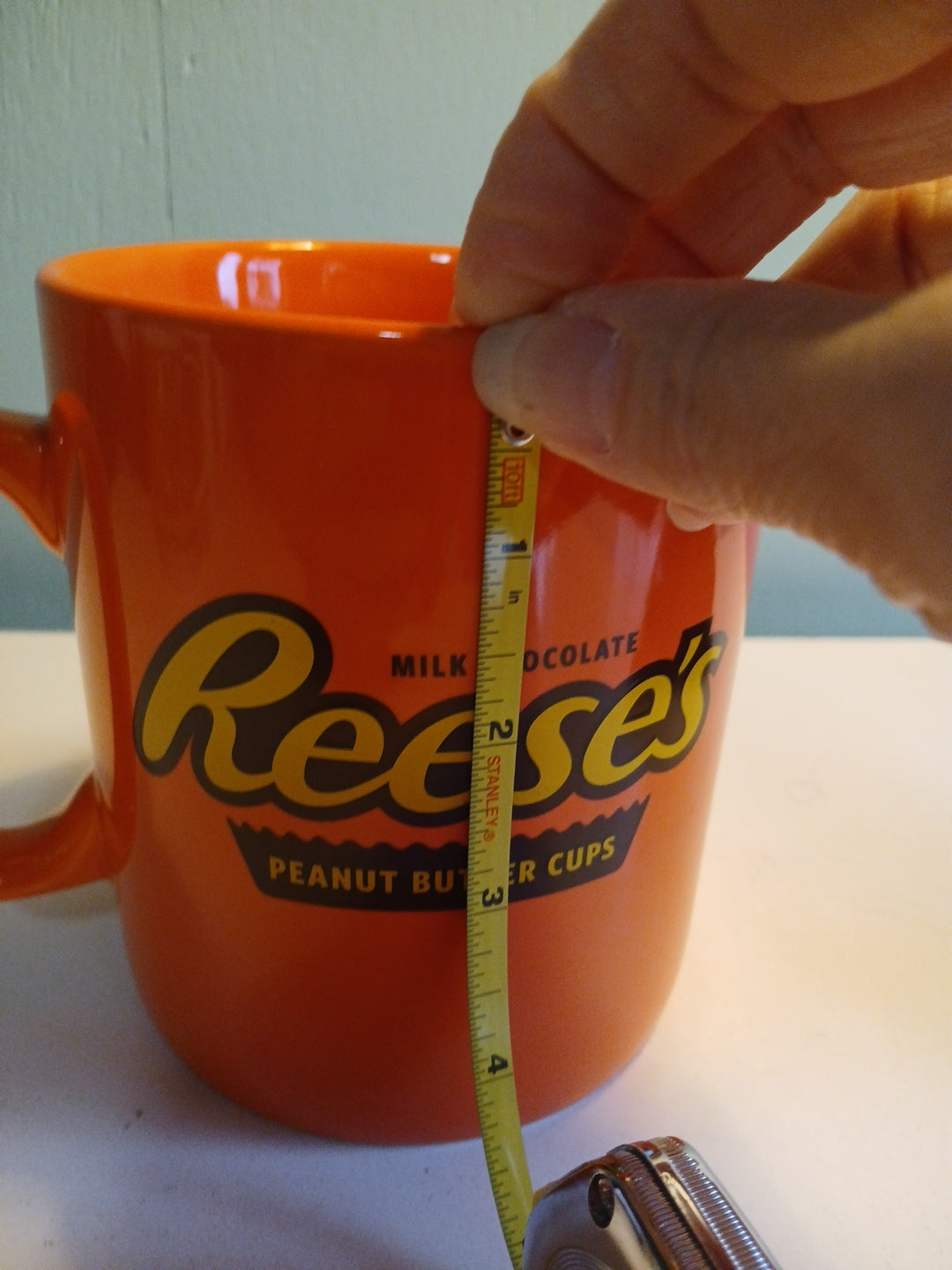 Orange mug with Reese's logo being measured with a tape measure.