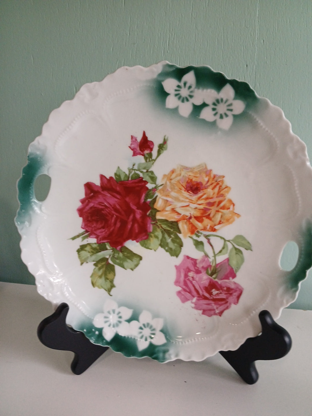 Decorative plate with floral design on a stand against a light green wall.