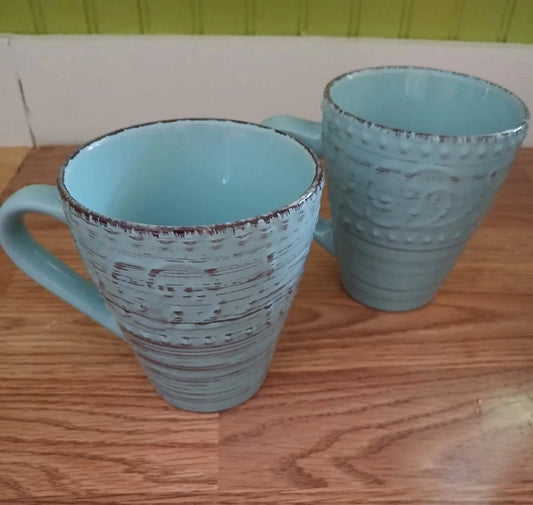 Two light blue ceramic mugs with textured design on a wooden surface.