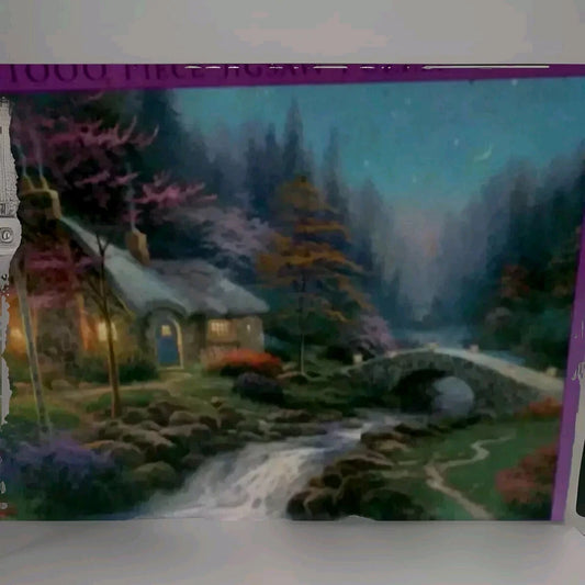 Framed artwork of a cozy cabin with a bridge and trees in a forest setting.